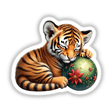 Tiger Cub Sleeping on Christmas Ornament: A charming depiction of a tiger cub gently holding and resting atop a festive Christmas ornament, available as unique stickers or digital artwork from Decal Venue.