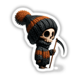 Whimsical skeleton gnome holding a tiny scythe, in a knitted black and orange outfit with a pom-pom hat.