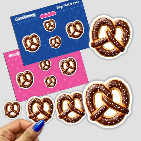 Hand holding Pretzel Shaped Cookie with Brown Icing and Salt Details sticker pack, with close-up of chocolate covered pretzels with sprinkles and a white plate in the background.