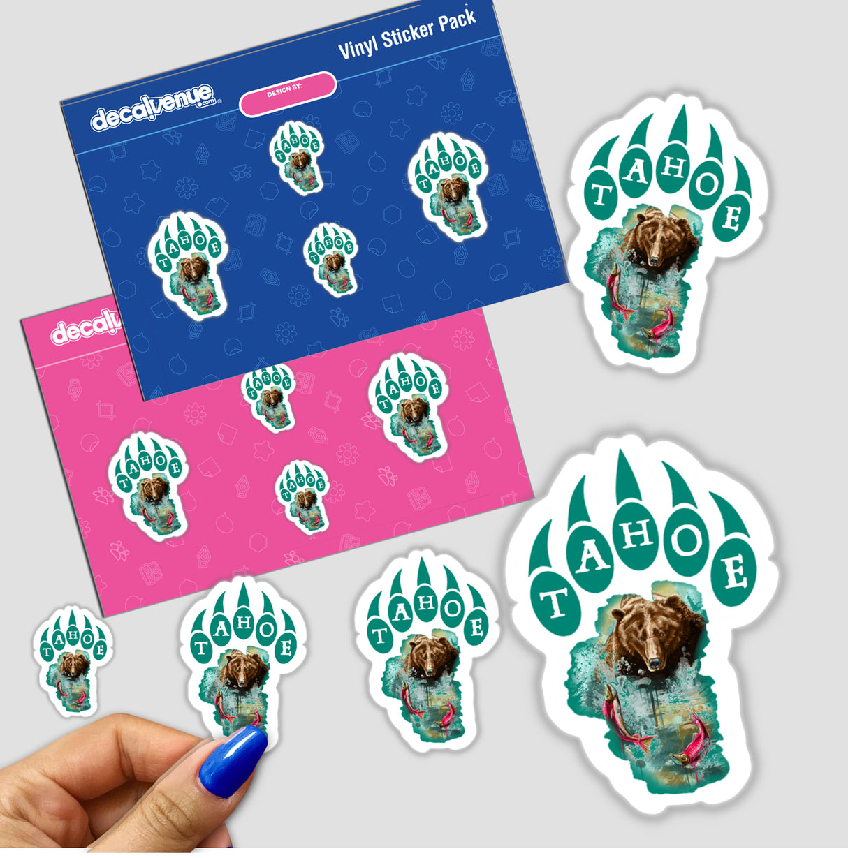 Tahoe Bear Print sticker features a cartoon bear holding a fish, available as a sticker or digital artwork. A close-up shows a hand with blue nail polish holding the sticker.