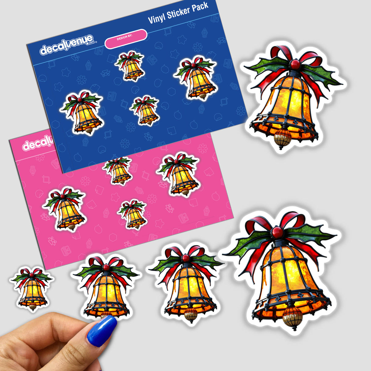 Christmas Bell Stained Glass Style sticker pack, featuring bell designs with ribbons, is held in a hand with blue nail polish, highlighting its unique, artistic detail from Decal Venue.