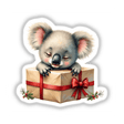 Baby Koala Sleeping on Christmas Present Box, depicted as a cartoonish koala resting atop a wrapped gift, available as stickers or digital artwork, reflecting Decal Venue's unique style.